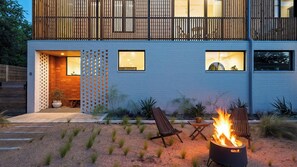 Ein modernes, zweistöckiges Haus mit blauer Fassade, einem hölzernen Balkon und einer Feuerstelle im Vordergarten.