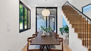 A modern dining area with a wooden table, chairs, and a staircase with wooden steps and metal railings. - Elizabeth House by Avantstay Saltwater Plunge Pool + Casita + Firepit (Austin)