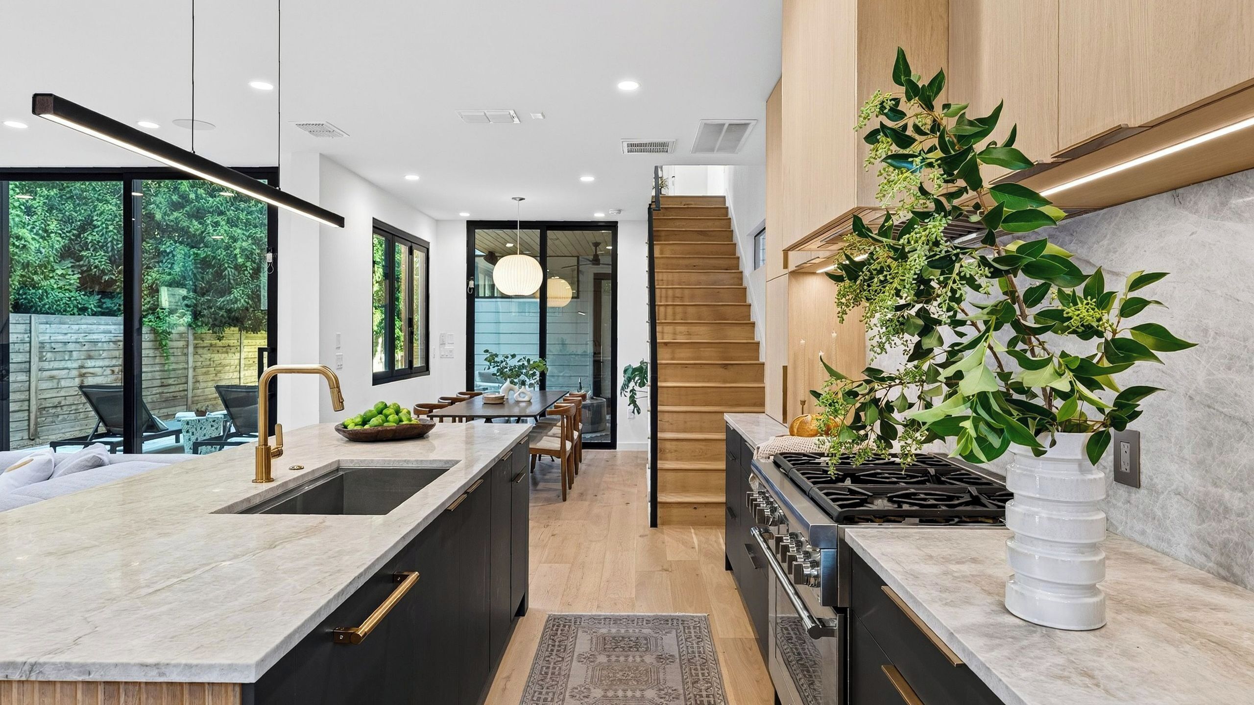 A modern kitchen with a central island, a dining area with a wooden table, and a staircase leading to an upper level.