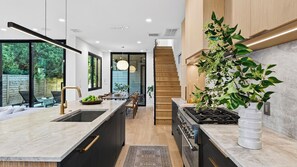 Una cocina moderna con una isla central, un comedor con mesa de madera y una escalera que sube a un nivel superior.