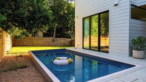Una piscina rectangular con un flotador circular, rodeada por un muelle de madera y un césped.
