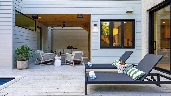 Un patio moderno al aire libre con piscina, sillas de descanso y zona de barbacoa.