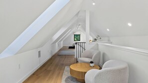 Amplia habitación en ático con techo inclinado, suelo de madera y un rincón de estar con dos sillones y una mesa redonda.