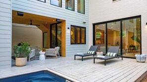 Una terraza moderna al aire libre con sillones de descanso, una piscina pequeña y un área de comedor con paredes de vidrio.