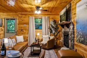 A cozy log cabin interior with a sofa, armchairs, a fireplace, and a dining area. - Havenheart Smoky Mtns Romantic Treehouse (Sevierville)