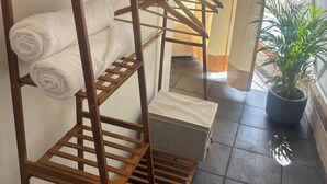 Una estantería de madera con toallas y una planta, ubicada cerca de una ventana con cortinas.