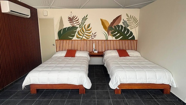 Habitación de hotel con dos camas, cabecera de madera, un mural en la pared y piso de baldosas.