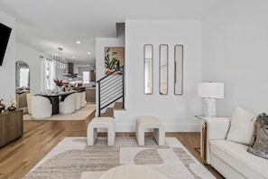 A modern living room with a staircase, a dining area, and a kitchen in the background. - Ovation @ The New Cumberland Resort (Nashville)