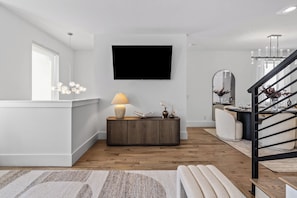 A modern living room with a flat-screen TV, a wooden console table with a lamp, and a staircase with a railing. - Ovation @ The New Cumberland Resort (Nashville)