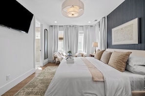 A modern bedroom with a large bed, a flat-screen TV, a wall-mounted artwork, and a view of the outdoors. - Ovation @ The New Cumberland Resort (Nashville)