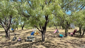 Un'area all'aperto con alberi, una struttura giochi, una sedia rossa e una bicicletta.
