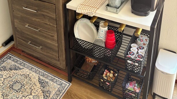 Una cucina compatta con lavello, macchina per caffè e scaffale metallico con diversi utensili da cucina.