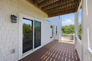 Eine überdachte Terrasse mit Holzboden und weißen Geländern, die zu einer Glastür führt.