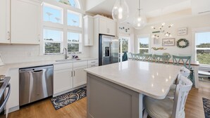 A modern kitchen with white cabinetry, a stainless steel refrigerator, and a large island. - Coastal Escape, Pool, Hot Tub & Resort Amenities (Currituck County)