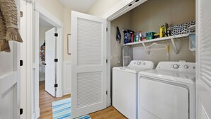 A laundry room with two white washing machines, a drying rack, and a shelf with cleaning supplies. - Coastal Escape, Pool, Hot Tub & Resort Amenities (Currituck County)