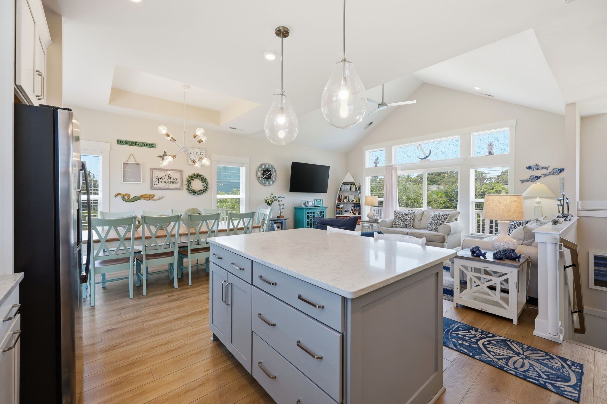 A spacious kitchen with a large island, dining area with chairs, and a living room with a sofa and TV.