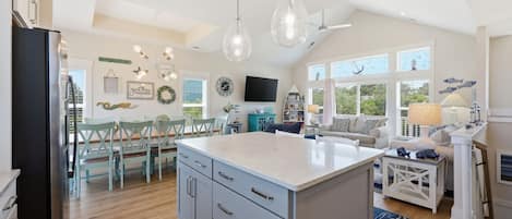 Una cocina amplia con una isla grande, comedor con sillas y sala de estar con sofá y televisor.