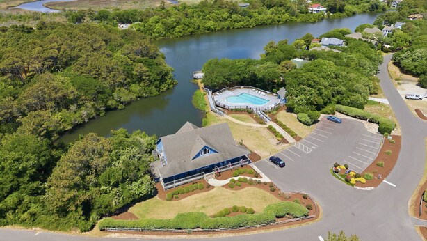 An aerial view of a resort with a swimming pool, a large building, and a parking area. - Coastal Escape, Pool, Hot Tub & Resort Amenities (Currituck County)