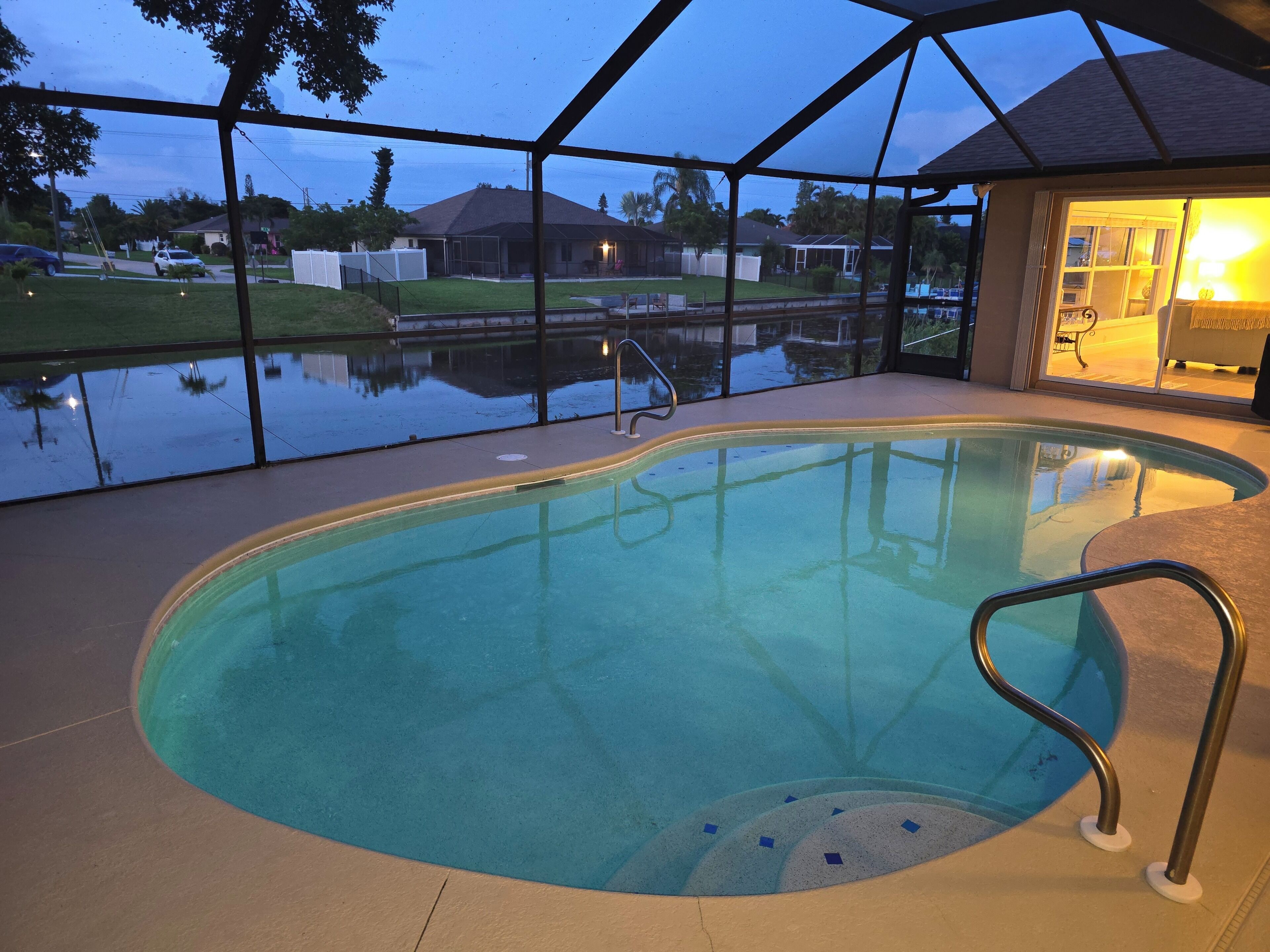 An indoor swimming pool with clear water, surrounded by a covered area with a view of the neighborhood.