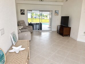 Una sala de estar con sofá, televisión sobre un mueble y vistas al exterior a través de una puerta de vidrio.
