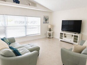 Una sala de estar con un sofá, un televisor sobre un mueble bajo y una ventana con persianas.
