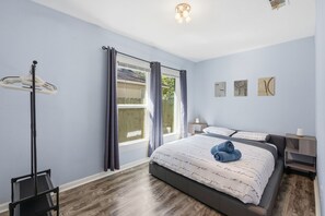 A bedroom with a bed, a nightstand, a lamp, a window with curtains, and artwork on the wall. - HydePark Stay  UT Modern 2BR/1.5BA Yard & Parking (Austin)