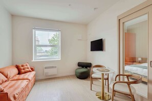 A modern room with a sofa, a small table with chairs, a bed, and a window with blinds. - 117 Cook - Apartment in Old Quebec (Québec)