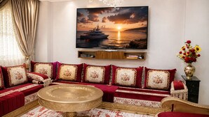 A luxurious living room with a large sofa set, a round coffee table, and a painting of a sunset over the sea.