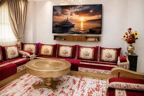 A luxurious living room with a large sofa set, a round coffee table, and a painting of a sunset over the sea.