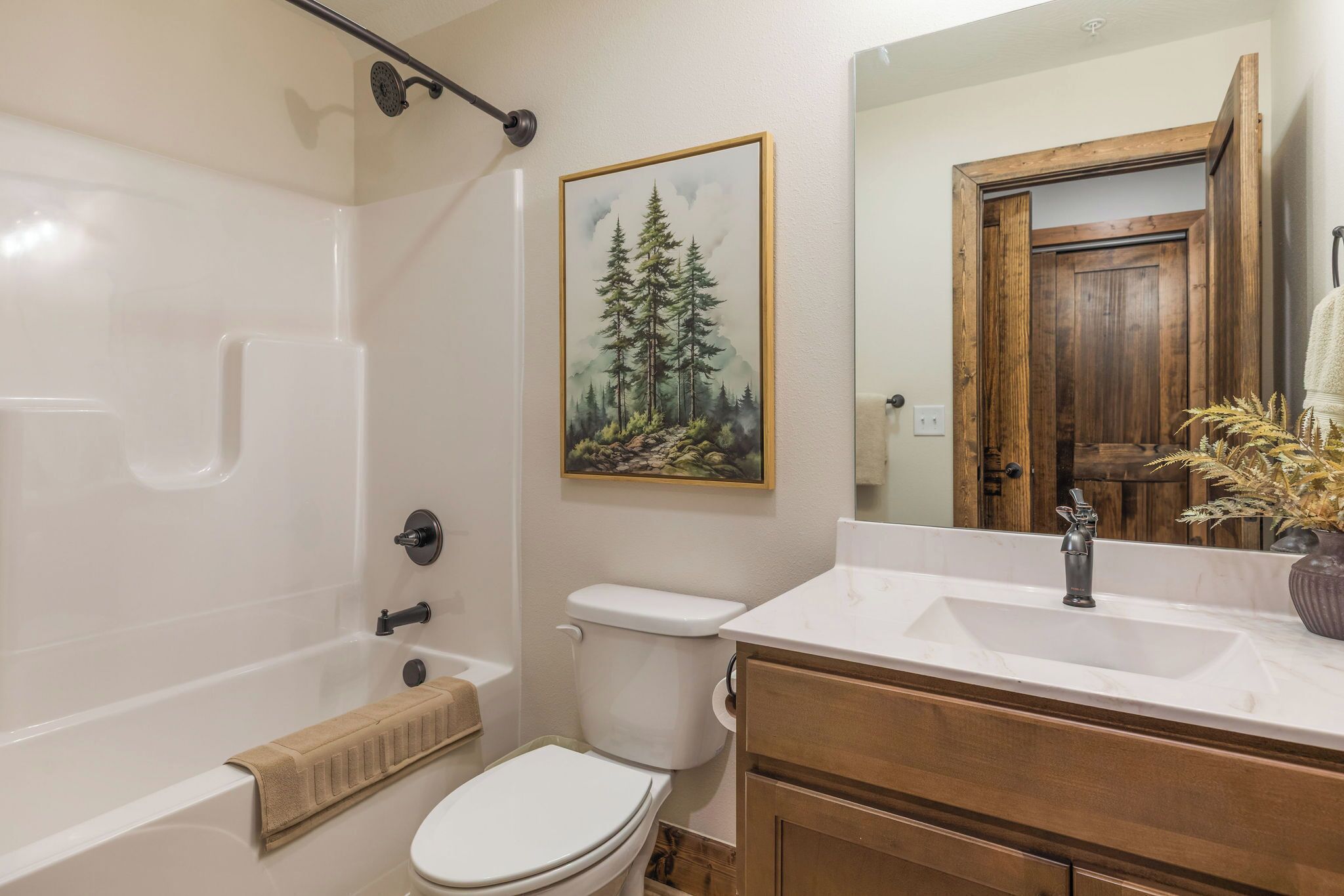 Un baño con bañera, inodoro, lavamanos y un cuadro de un bosque.