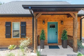 A wooden cabin with a front porch, a blue door, and two potted plants.