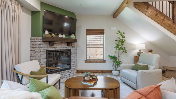 A cozy living room with a stone fireplace, a flat-screen TV mounted above it, and a comfortable seating area with a sofa and chairs.