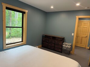 A bedroom with a large window, a bed, a dresser, and a door.