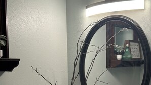 Een badkamer met een witte wastafel, twee kraanwerkstukken, een spiegel, een vaas met takken en een handdoekhouder.