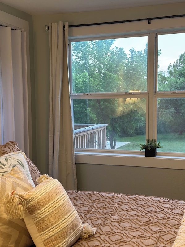 A bedroom with a large window, a bed with patterned bedding, and a small potted plant on the windowsill.