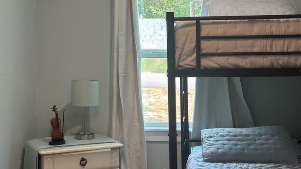 Een slaapkamer met een stapelbed, een nachtkastje met een lamp en een dressoir.