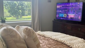 Een slaapkamer met een bed, een televisie op een dressoir en een raam met uitzicht op bomen.
