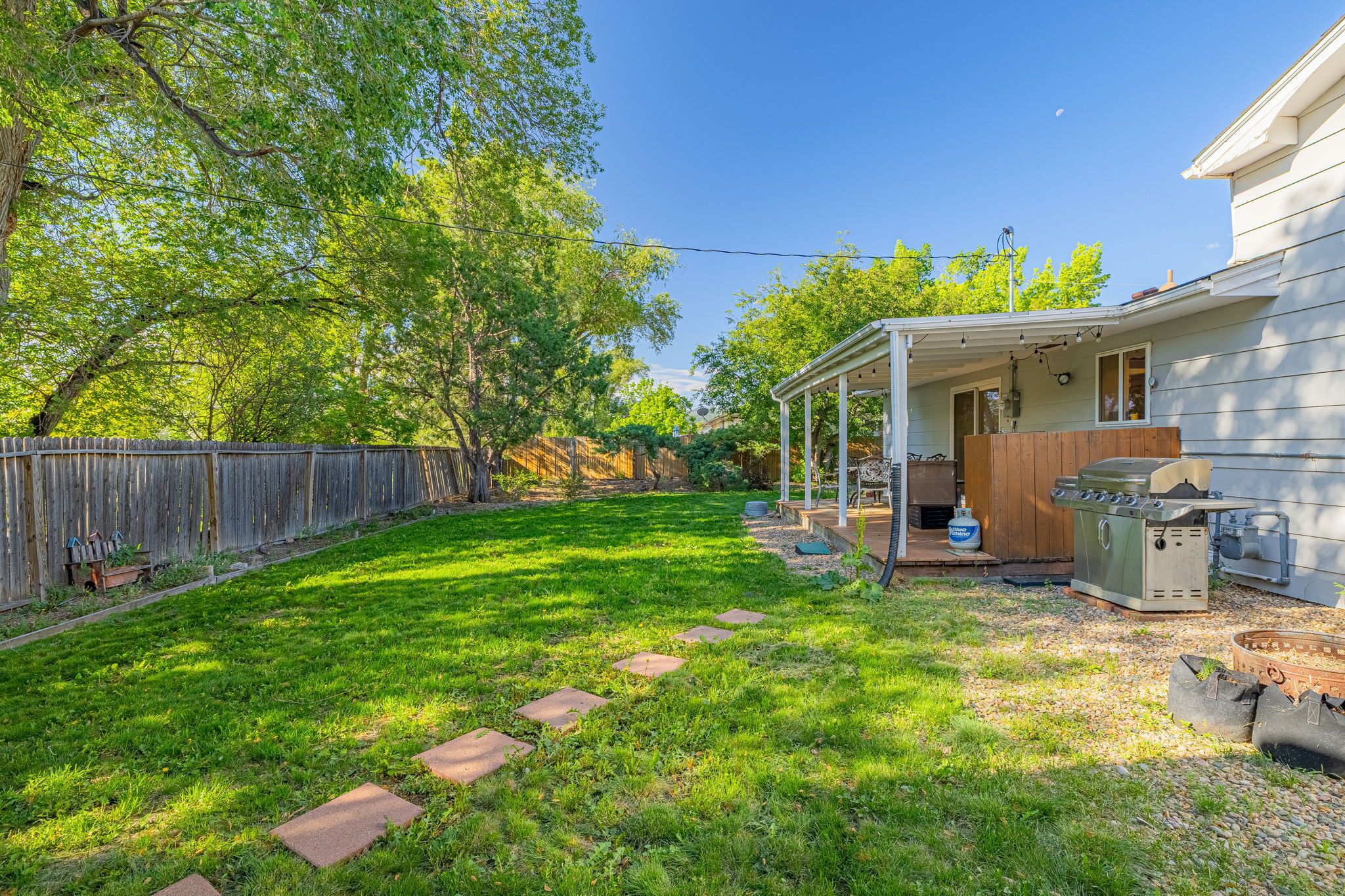 A backyard with a covered patio, a barbecue grill, and a wooden fence.