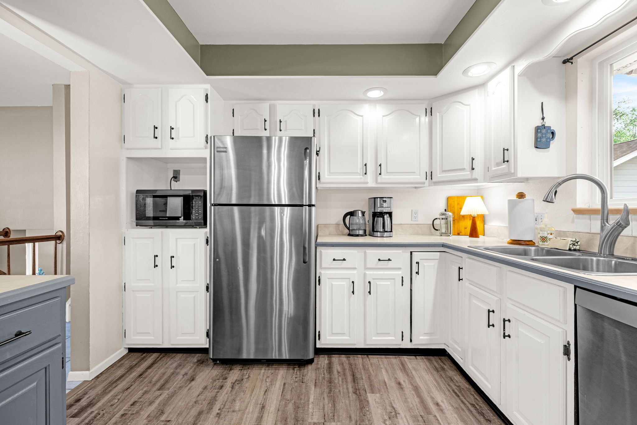 Una cocina moderna con armarios blancos, un refrigerador de acero inoxidable, un microondas, una cafetera y un fregadero.