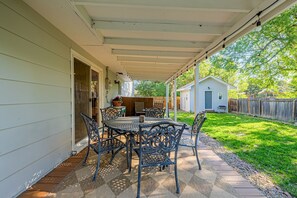 Eine überdachte Terrasse mit Tisch und Stühlen, einem Grill und einem Haus im Hintergrund.
