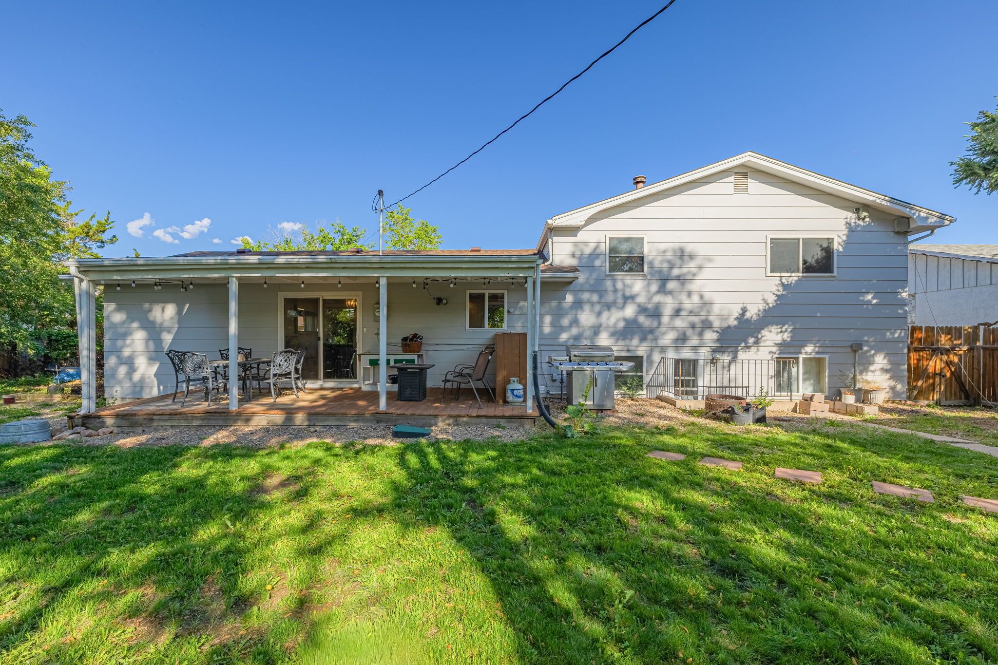 A two-story house with a covered patio area, a barbecue grill, and a fenced yard.