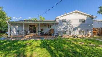 A two-story house with a covered patio area, a barbecue grill, and a fenced yard.
