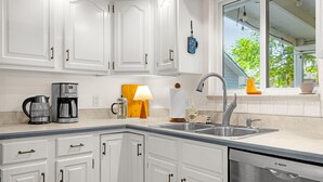 A kitchen with white cabinets, a Bosch dishwasher, a coffee maker, and a window with a view of trees. - Garden of the Gods Cottage-4B/3b Pioneer Park (Colorado Springs)
