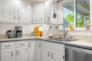 A kitchen with white cabinets, a Bosch dishwasher, a coffee maker, and a window with a view of trees. - Garden of the Gods Cottage-4B/3b Pioneer Park (Colorado Springs)