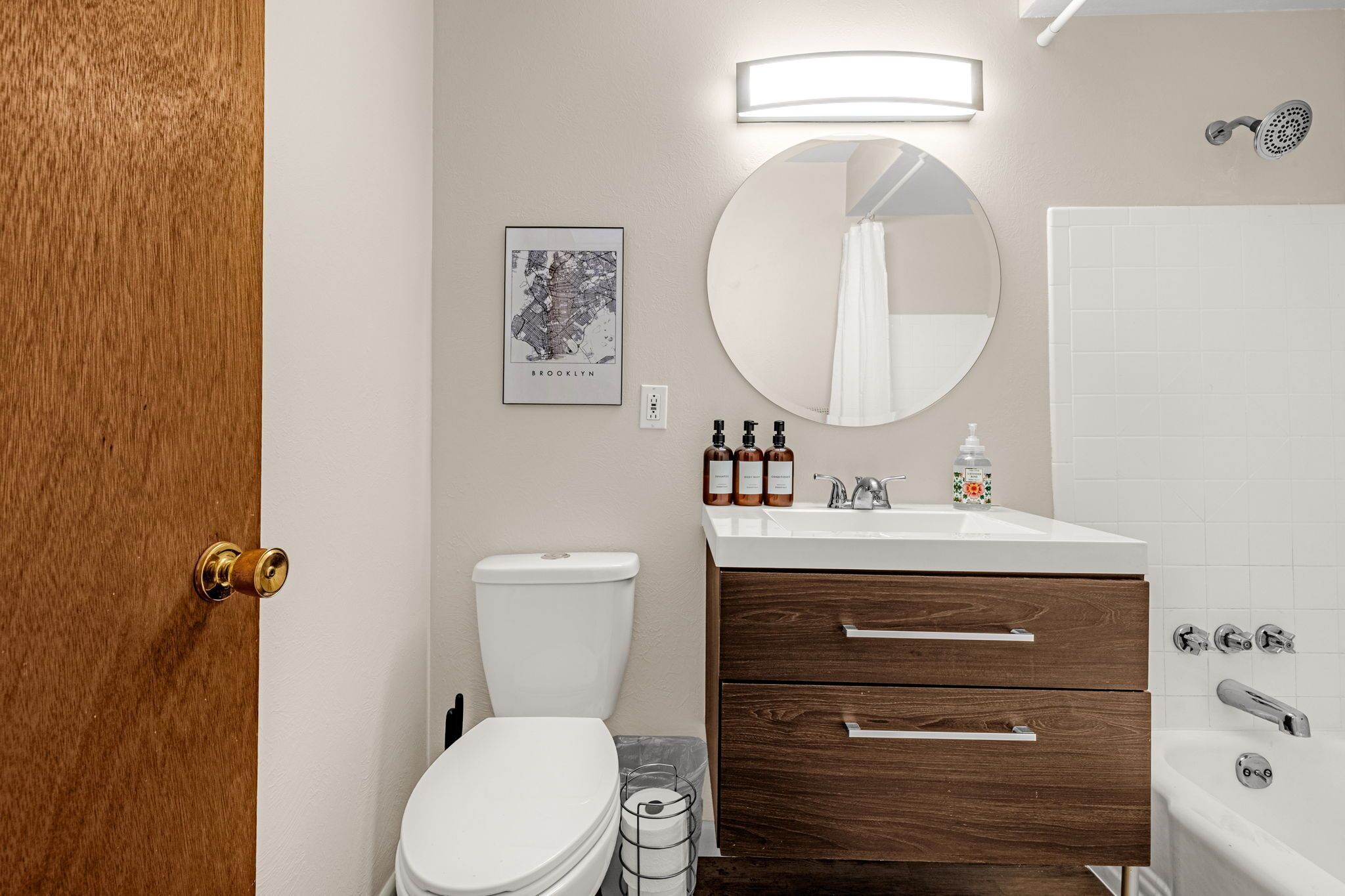A bathroom with a toilet, a sink with soap dispensers, a mirror, and a shower.