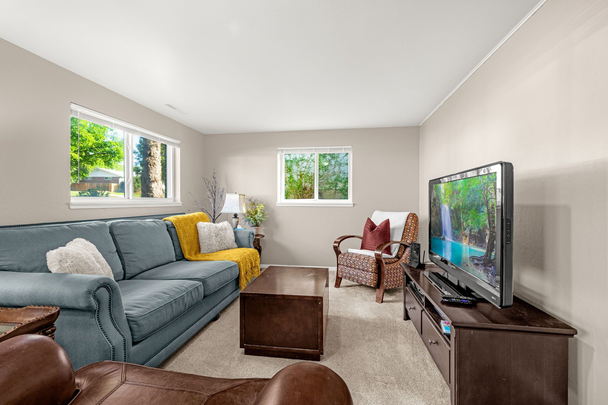 A living room with a sofa, coffee table, TV, and two windows.
