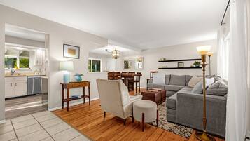 A modern living room with a grey sofa, a wooden coffee table, and a dining area with a wooden table and chairs.