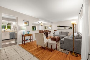 Een moderne woonkamer met een grijze bank, een houten salontafel, en een eethoek met een houten tafel en stoelen.