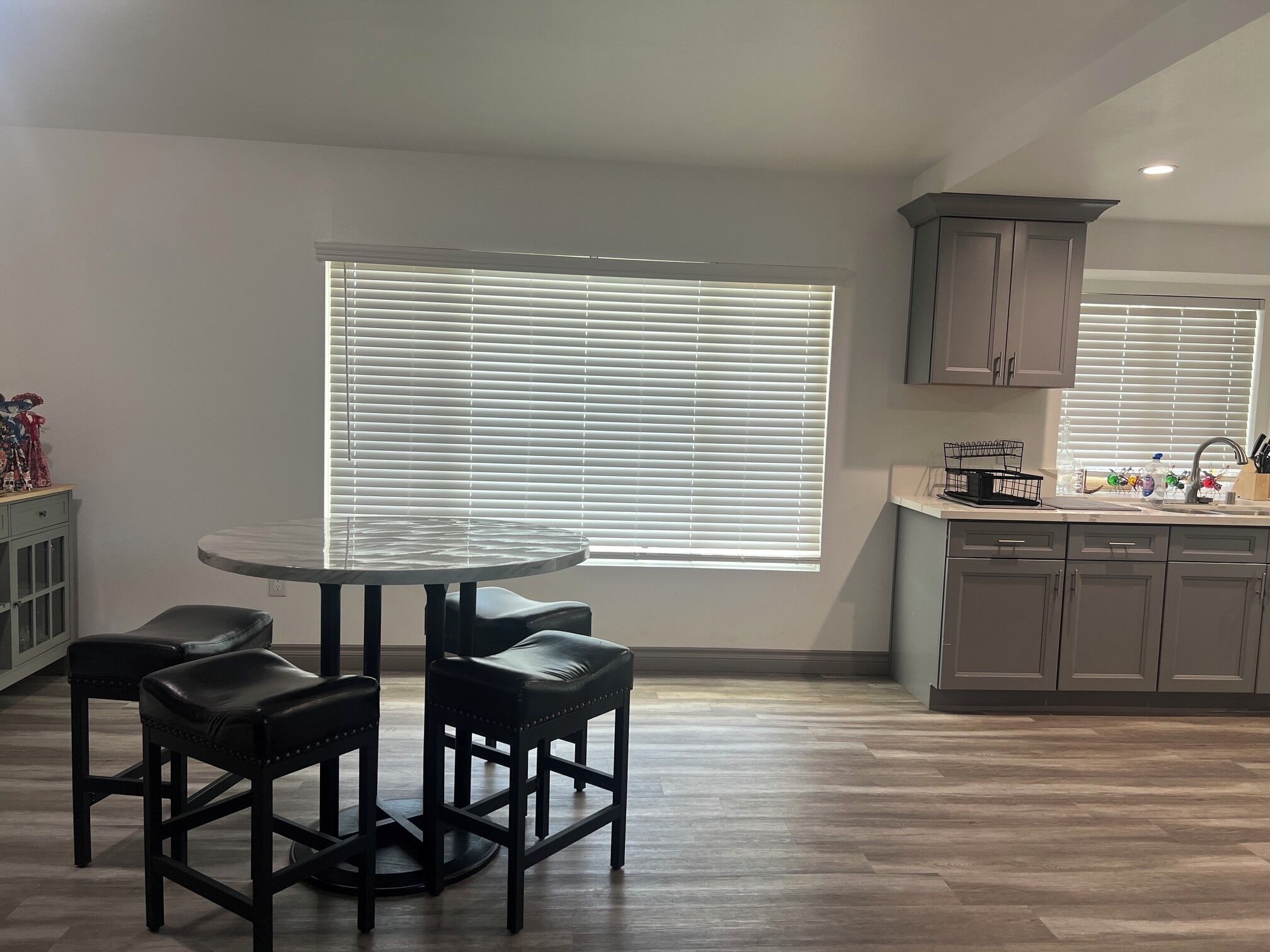 Una cocina con una mesa redonda y cuatro sillas, una ventana con persianas, y un armario sobre el lavabo.