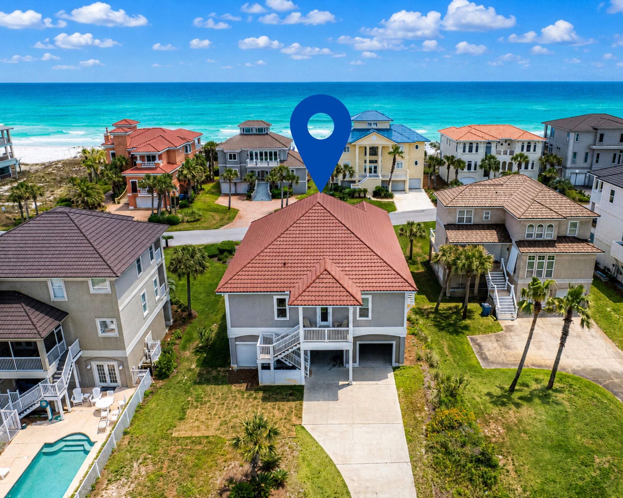 A residential area with a large house featuring a red roof, a pool, and a view of the ocean.
